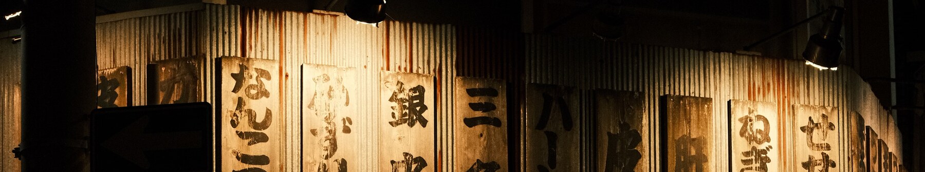 暖色の灯りに照らされたトタン壁と木の看板が並ぶ、夜の店先のイメージ写真